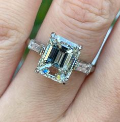 a woman's engagement ring with an emerald and baguette cut diamond in the center