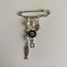 a brooch with charms attached to it on a white surface and one has a fish charm