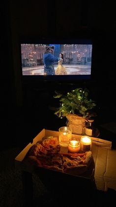 a pizza sitting on top of a table in front of a tv with candles around it