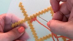 two hands are stitching together on a piece of fabric with orange thread and needles