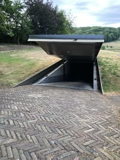 an open metal door on the side of a brick road with grass and trees in the background