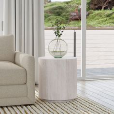 a living room with a couch, chair and glass vase on the end table in front of a sliding glass door