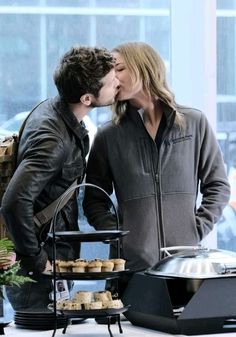 a man and woman kissing while standing in front of a table with cupcakes