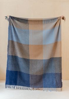 a blue and tan checkered blanket with fringes on the bottom, hanging from a wall