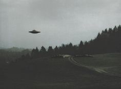 an alien flying over a lush green forest covered hillside next to a road with cars driving on it