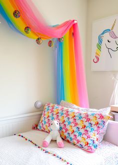 a bed with a rainbow canopy over it and a unicorn stuffed animal on the pillow