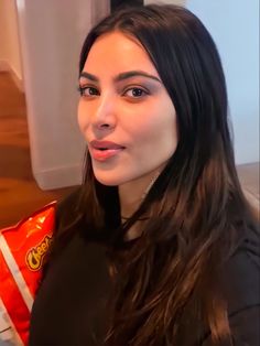 a woman with long dark hair is looking at the camera while holding a candy bar in her hand