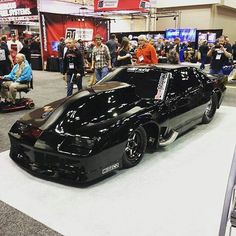 a black car is on display in a showroom with people looking at the cars