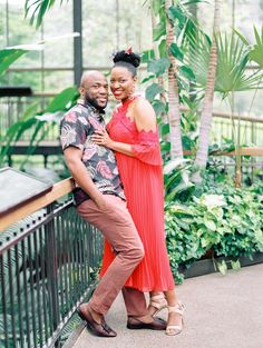 a man and woman standing next to each other in front of some palm trees with their arms around each other