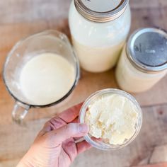 a person is holding a spoon in front of two jars filled with cream on a wooden table