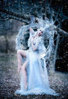 a woman dressed as an angel sitting in the snow with her legs spread out and wings outstretched