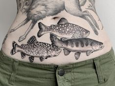 a woman's stomach with fish and deer tattoos on her belly, while the lower part of her body is covered in green pants