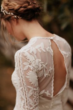 the back of a woman's wedding dress with white lace on it and flowers in her hair