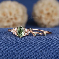 a ring with an oval green stone surrounded by leaves and flowers on top of a blue cloth