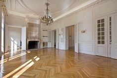 an empty room with white walls and wood floors, chandelier and fireplace in the center