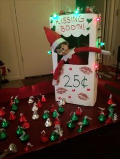 an elf is sitting in front of a sign that says kissing booth 25 cents on it