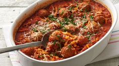 a white dish filled with meatballs and pasta on top of a towel next to a spoon