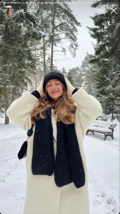 a woman standing in the snow with her hands on her head wearing a hat and scarf