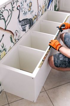 a man in orange gloves working on an unfinished cabinet with drawers and tools inside it