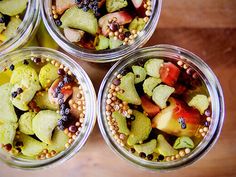 four glass jars filled with different types of fruits and vegetables on top of a wooden table