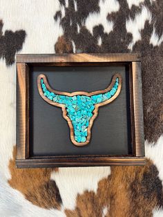 a longhorn skull with turquoise beads in a wooden frame on a cow print background