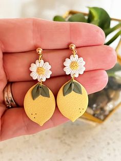 a pair of yellow earrings with white flowers and leaves on the end of each dangle