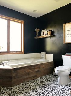 a white toilet sitting next to a bath tub in a bathroom under a window on top of a tiled floor