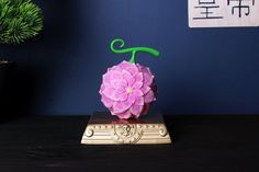 a pink flower sitting on top of a wooden table next to a potted plant