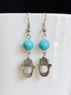 Turquoise and Hamsa Hand Dangle Earrings hang 2 inches from the ear. The beautiful turquoise blue compliments the silver details perfectly.  The Hamsa Hand is an ancient Middle Eastern symbol for the Hand of God. It is a protective sign, bringing its owner happiness, luck, health, and good fortune. Spiritual Turquoise Sterling Silver Earrings, Spiritual Turquoise Earrings With Natural Stones, Blue Spiritual Dangle Earrings, Spiritual Blue Dangle Earrings, Blue Spiritual Nickel-free Earrings, The Hand Of God, Red Coral Necklace, Hand Of God, Jasper Earrings