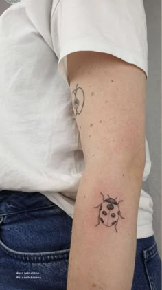 a ladybug tattoo on the left arm and right arm is shown in black ink