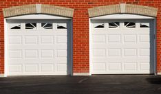 two white garage doors in front of a brick wall