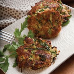 two crab cakes on a white plate with green garnishes and a fork