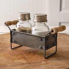 two salt and pepper shakers sitting in a metal caddy on a wooden table