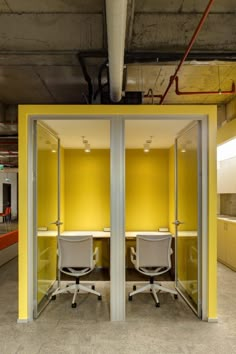 two office chairs sitting in the middle of a room with yellow walls and white desks