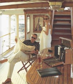 a man and woman on a boat reading the paper while another person sits in a chair