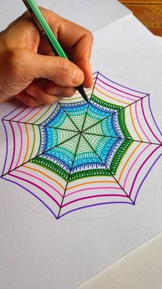 someone is drawing a spider web with colored pencils on top of the paper that they are holding