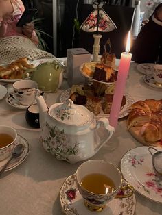 a table topped with tea cups and plates filled with food next to a lit candle