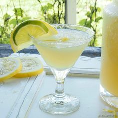 a glass filled with lemonade next to a pitcher and sliced lemons on a window sill