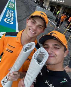 two men standing next to each other in front of a race track holding giant objects