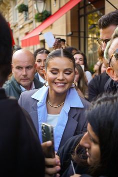 a group of people standing around each other in front of a building with one woman holding a cell phone