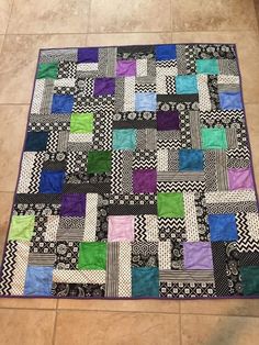 a black and white patchwork quilt with multi colored squares on the bottom, sitting on a tile floor