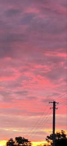 the sky is pink and purple as the sun sets in the distance behind power lines