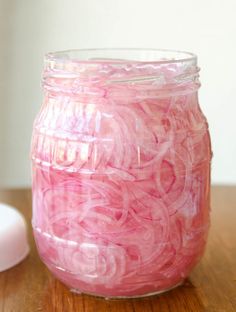 a jar filled with red onions sitting on top of a wooden table