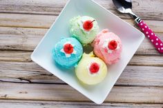 three different colored cupcakes on a white plate with a spoon and fork next to it