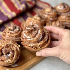 a person is holding some cinnamon rolls on a cutting board