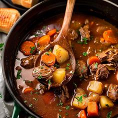 a pot filled with beef stew and carrots on top of a table next to cornbreads