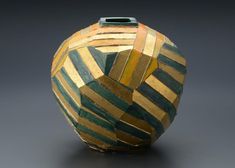 a decorative vase with gold and green stripes painted on it's sides, sitting on a gray surface