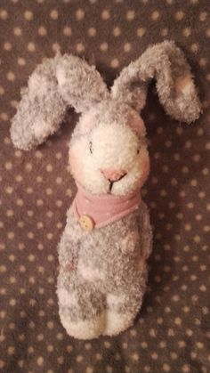 a small stuffed rabbit wearing a pink scarf on top of a polka dot bed sheet