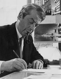 a man in suit and tie sitting at a desk writing on paper with a pen