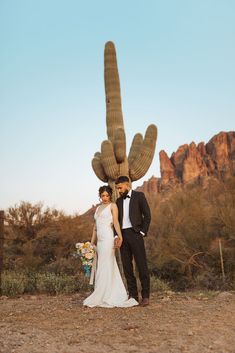 a bride and groom standing in front of a giant cactus